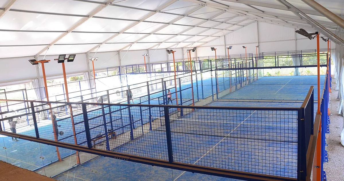 A padel player hitting the contrapared — using their own back glass wall to return the ball